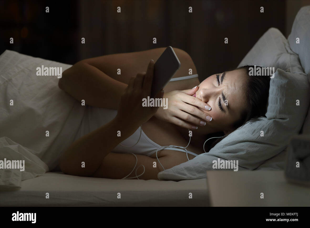 Worried woman watching bad online content in a smat phone lying on a bed in the night at home Stock Photo