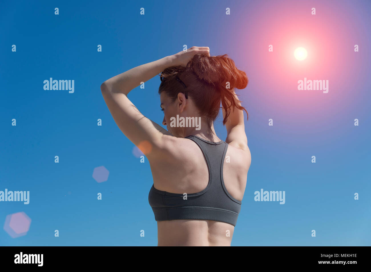 sporty woman wearing a sports bra tying her hair up before training Stock Photo