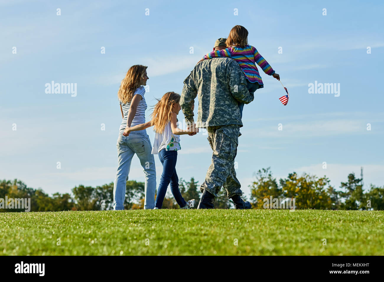 Back view soldier and his family are walking on the grass. Stock Photo