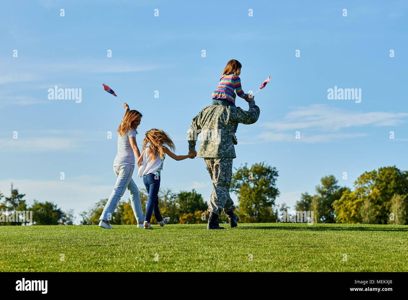 Soldier is walking with his family in the grass, back view. Stock Photo