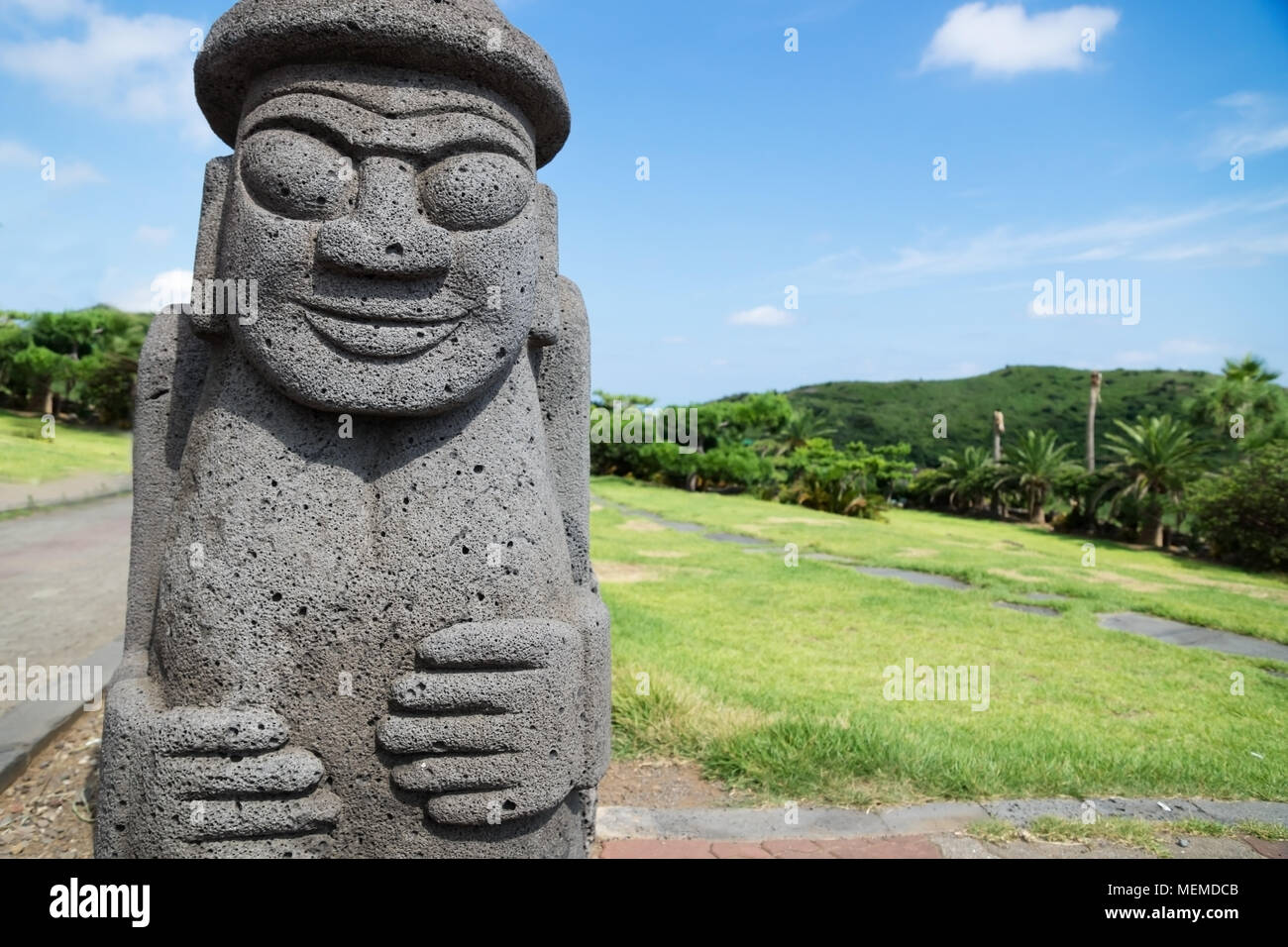 Dol Harubang statue in green grassland and trees in background at Yongmeori Beach, Sanbang-ro, Jeju Island, South Korea Stock Photo