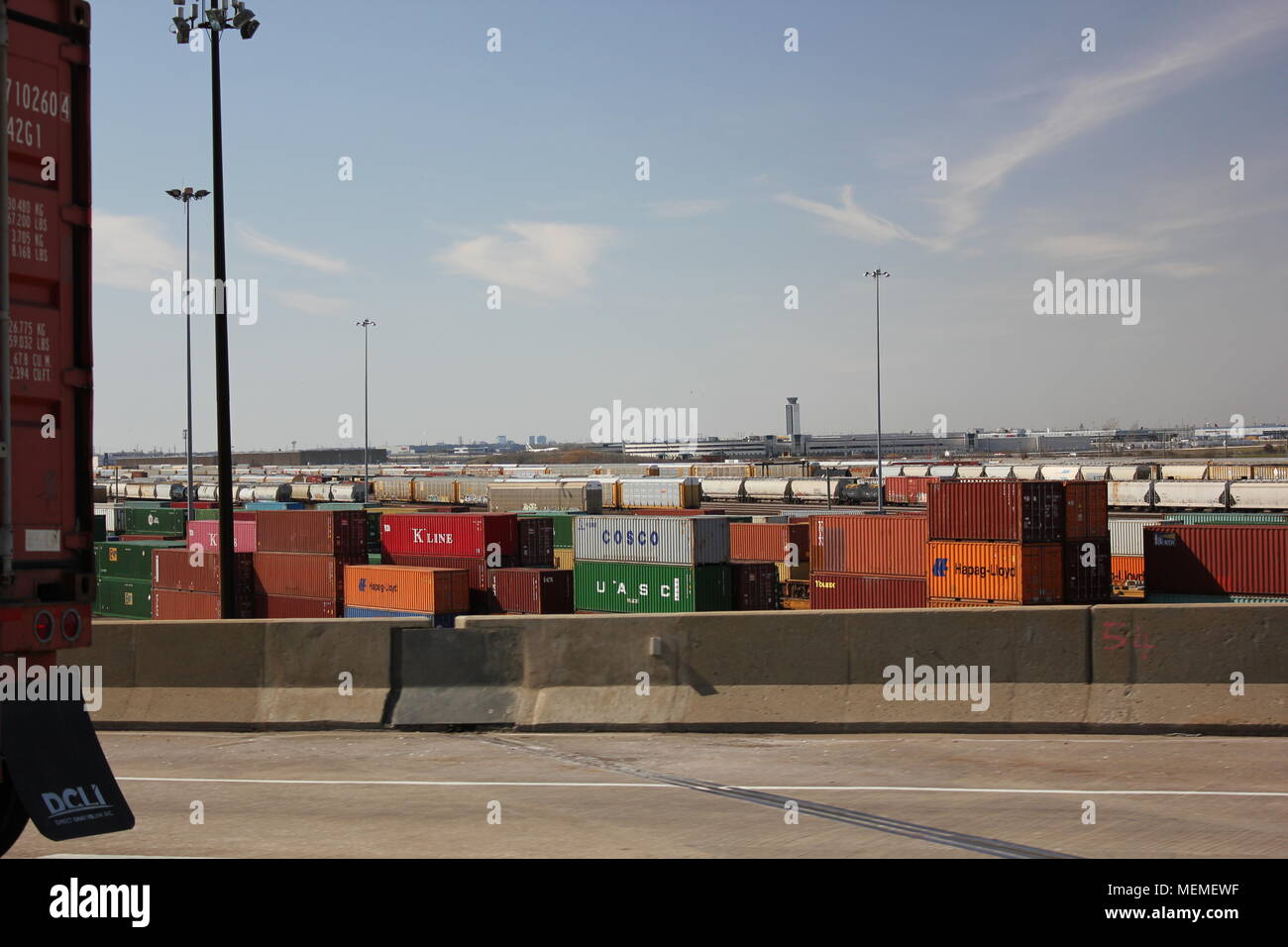 view of cargo shipping yard storage facility with a cargo box placed on a truck riding on a highway. Stock Photo
