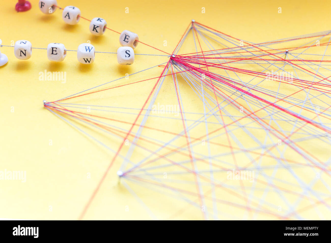 Lettered beads on rope and nails on yellow background visualizing fake news spread in network Stock Photo