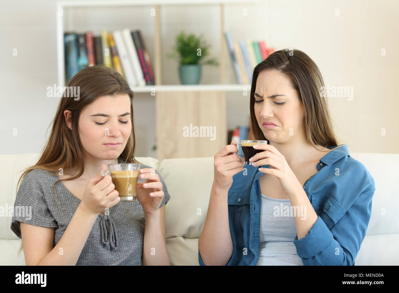 Two friends drinking coffee with bad flavour sititng on a couch in the living room at home Stock Photo