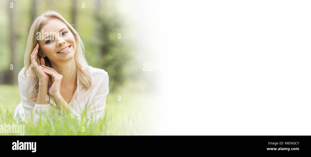 Blonde pretty girl laying on the grass in spring park and smiling ...