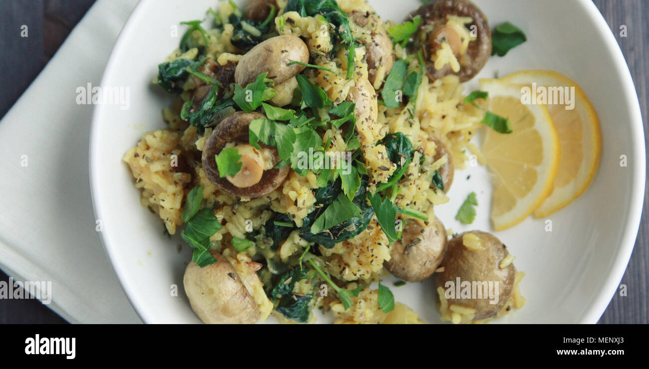 Yellow rice with mushrooms and spinach. Vegan dish. European cuisine. Vegetarian turmeric rice in the white bowl. Meatless. Wide photo. Top view. Stock Photo