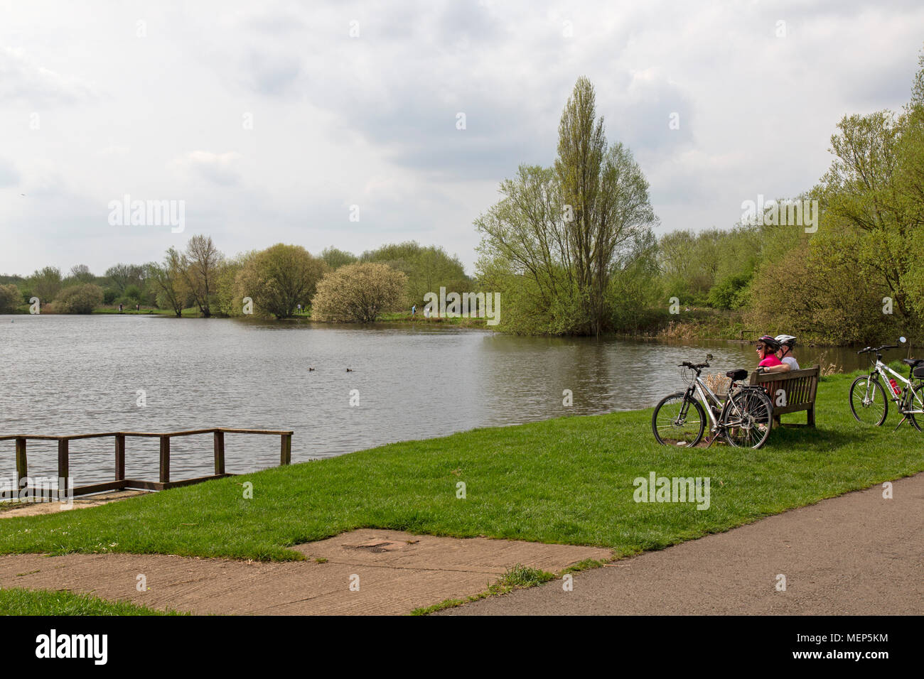 Watermead Country Park in Leicestershire, England. A middle aged couple take a rest on a bench after cycling around the lakes. Stock Photo
