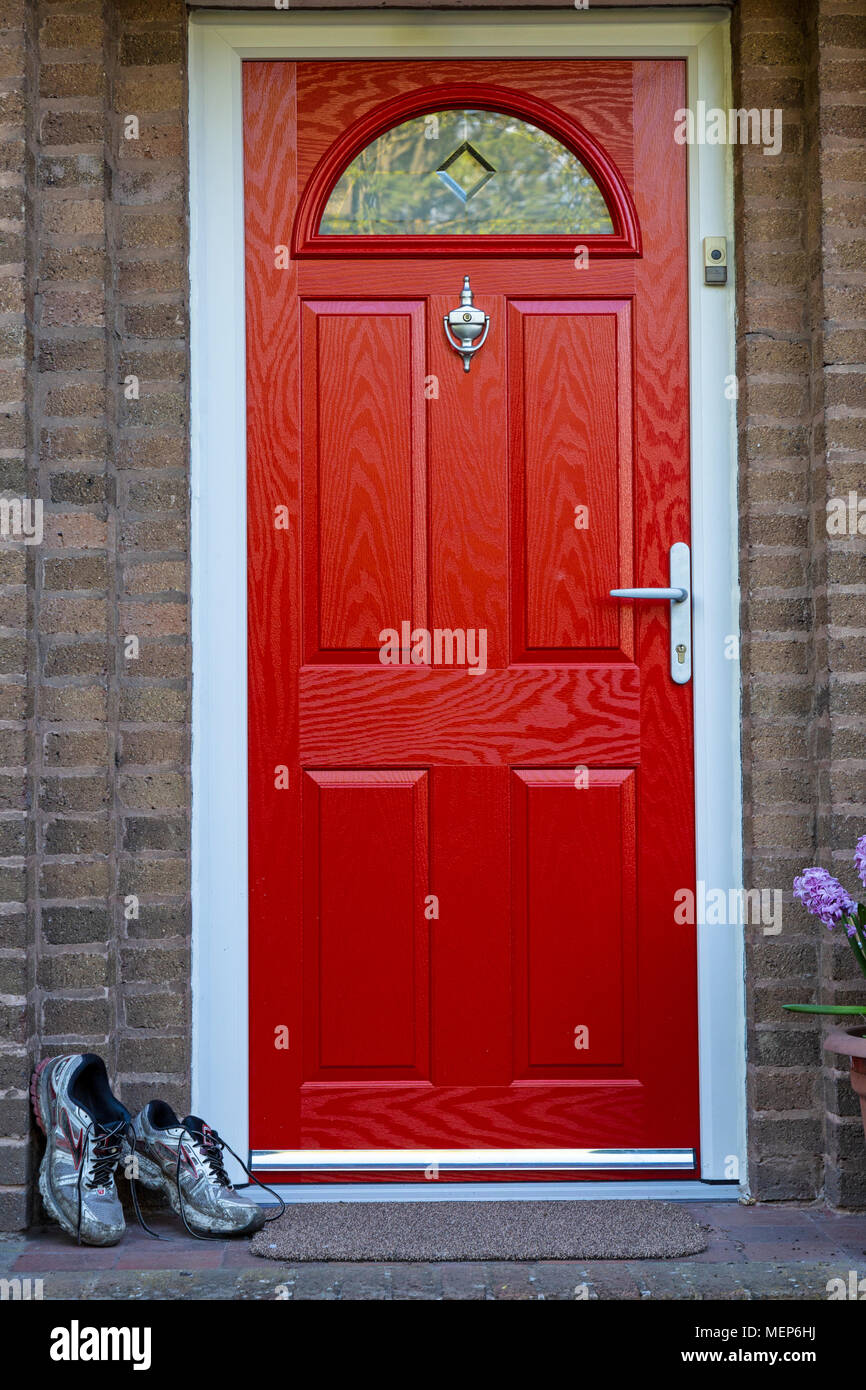 A pair of muddy running shoes left outside a house by a bright red door. Stock Photo