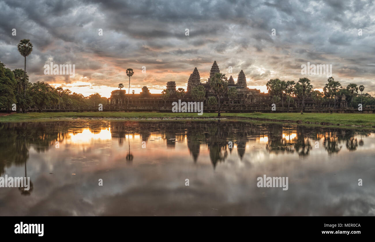 Cambodia ancient Temple Complex Angkor Wat at sunrise with dramatic clouds over the towers and reflection in the pond. Famous travel destination. Stock Photo