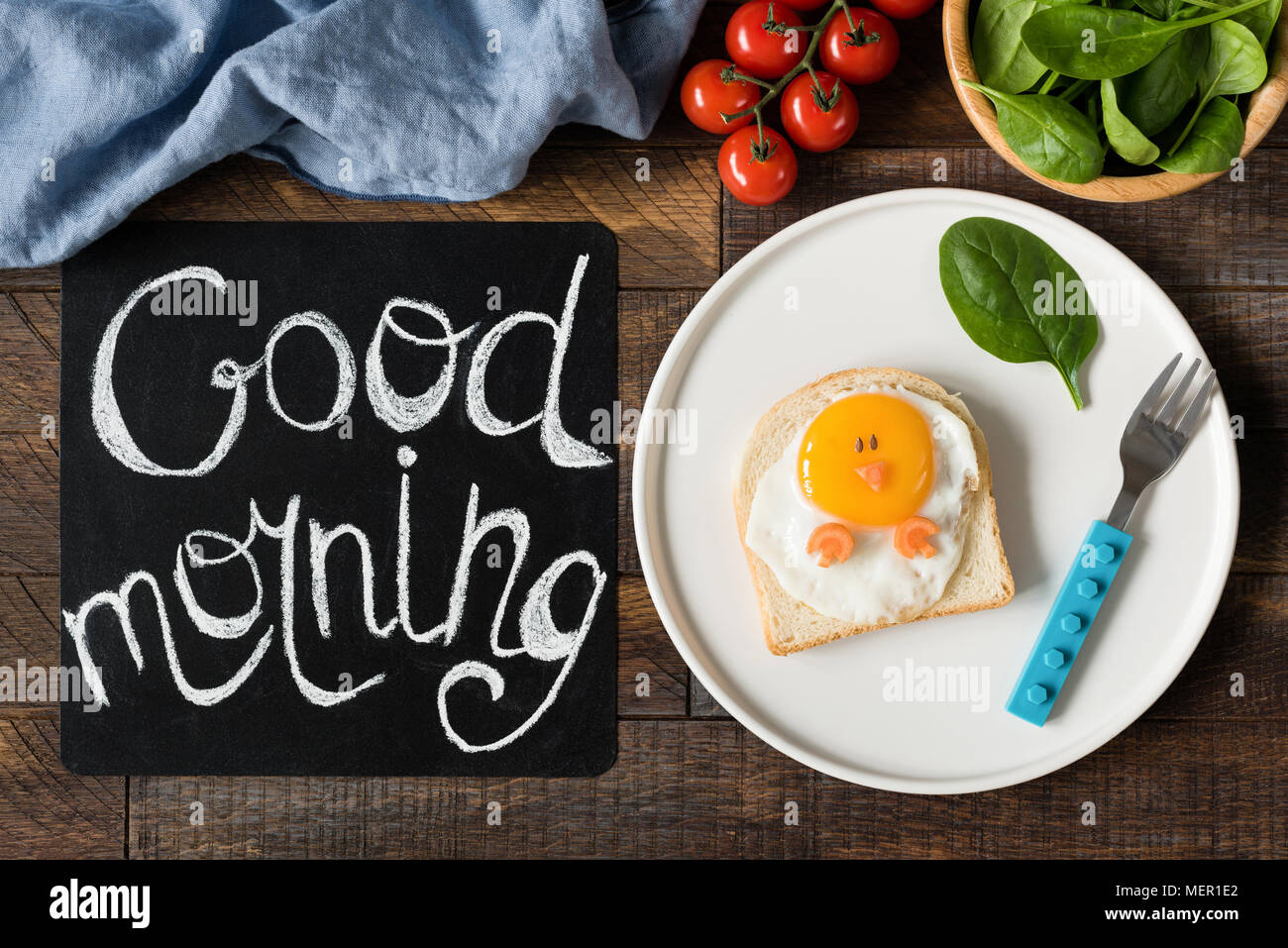 Funny sandwich chicken for kids on a plate. Black chalkboard with Good morning greeting, Healthy breakfast and healthy eating concept. Wooden table ba Stock Photo