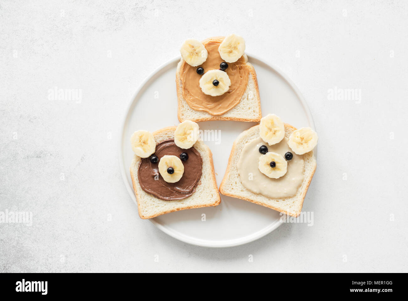 Funny animal face toasts with nut butter, banana and blueberries on white plate. Kids meal. Vegan, vegetarian, healthy lifestyle, healthy eating conce Stock Photo