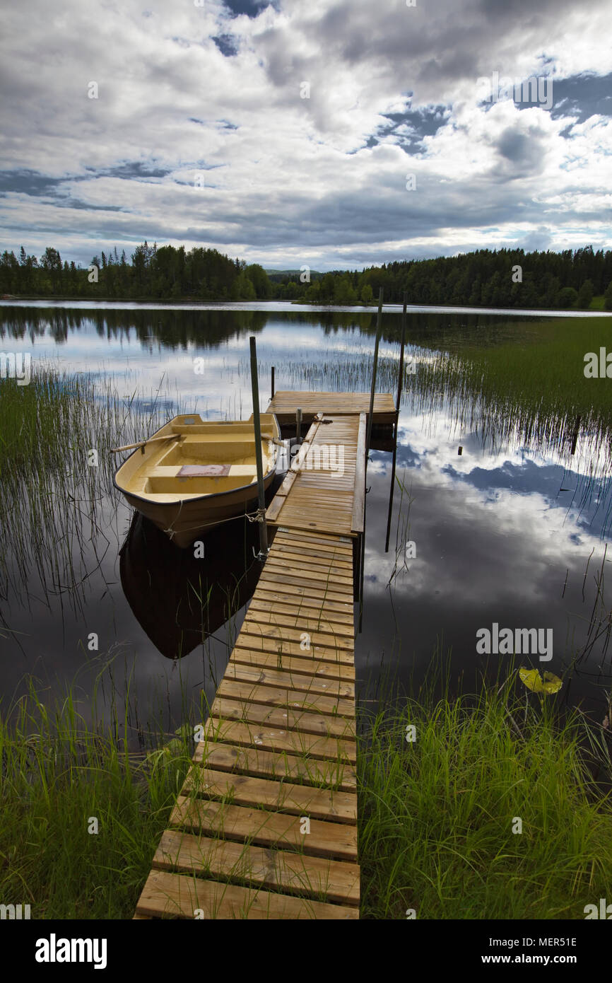 A rowing boat is moored at a jetty in a glassy forest lake Stock Photo ...