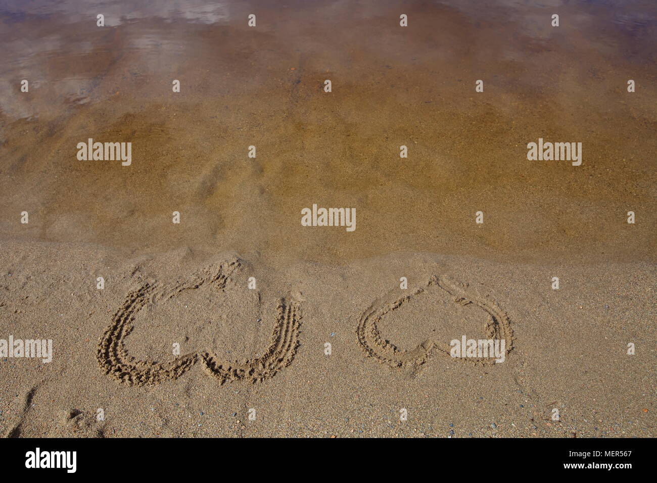 . Two hearts are drawn in the wet sand of a beach Stock Photo