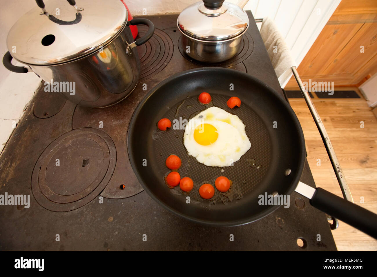 A fried egg is sizzling in a non-sticking frying pan together with cherry tomatoes. Stock Photo