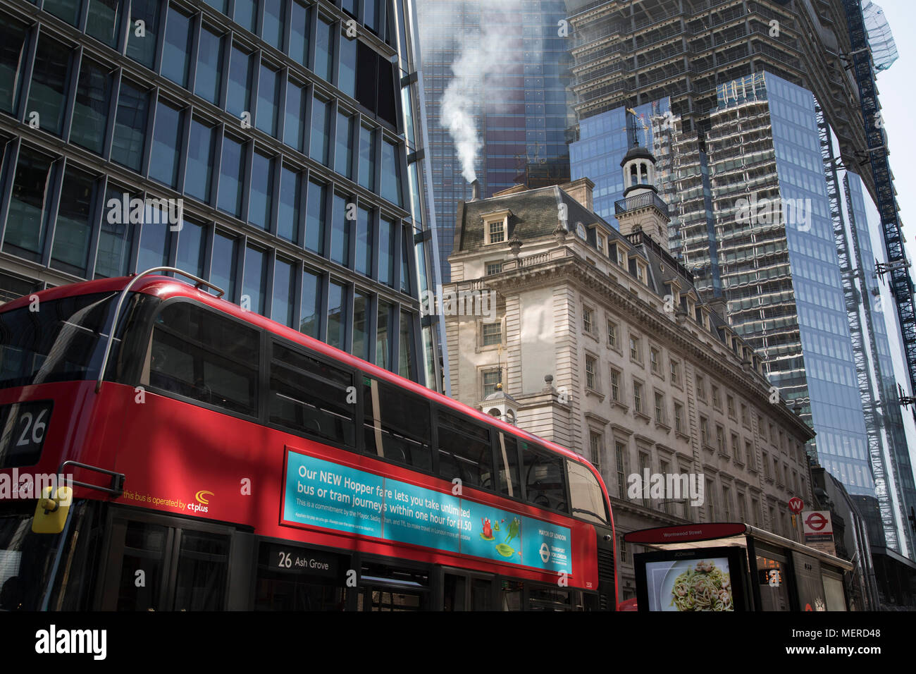 Pollution from the chimney of an old building pours out into the atmosphere amongst modern glass buildings in the City of London, London, England, United Kingdom. At street level, busses and traffic passes adding to the emissions, and all adding up to the poor air quality which people are breathing on a daily basis. London is trying to achieve air quality targets. The European Air Quality Index, run by the European Environment Agency EEA and the European Commission, allows users to check the current air quality across Europe’s cities and regions. Environmental groups called for the Government  Stock Photo