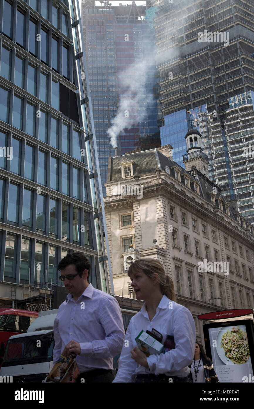Pollution from the chimney of an old building pours out into the atmosphere amongst modern glass buildings in the City of London, London, England, United Kingdom. At street level, traffic passes adding to the emissions, and all adding up to the poor air quality which people are breathing on a daily basis. London is trying to achieve air quality targets. The European Air Quality Index, run by the European Environment Agency (EEA) and the European Commission, allows users to check the current air quality across Europe’s cities and regions. Environmental groups called for the Government to take u Stock Photo