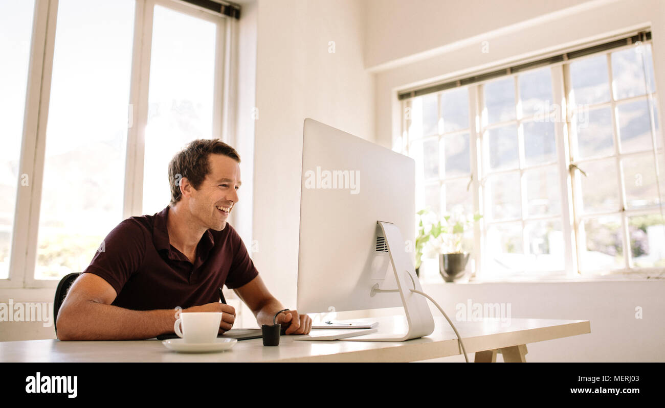 Smiling businessman working on computer and using a digitizer to make notes. Man sitting at his work table working on computer at home. Stock Photo