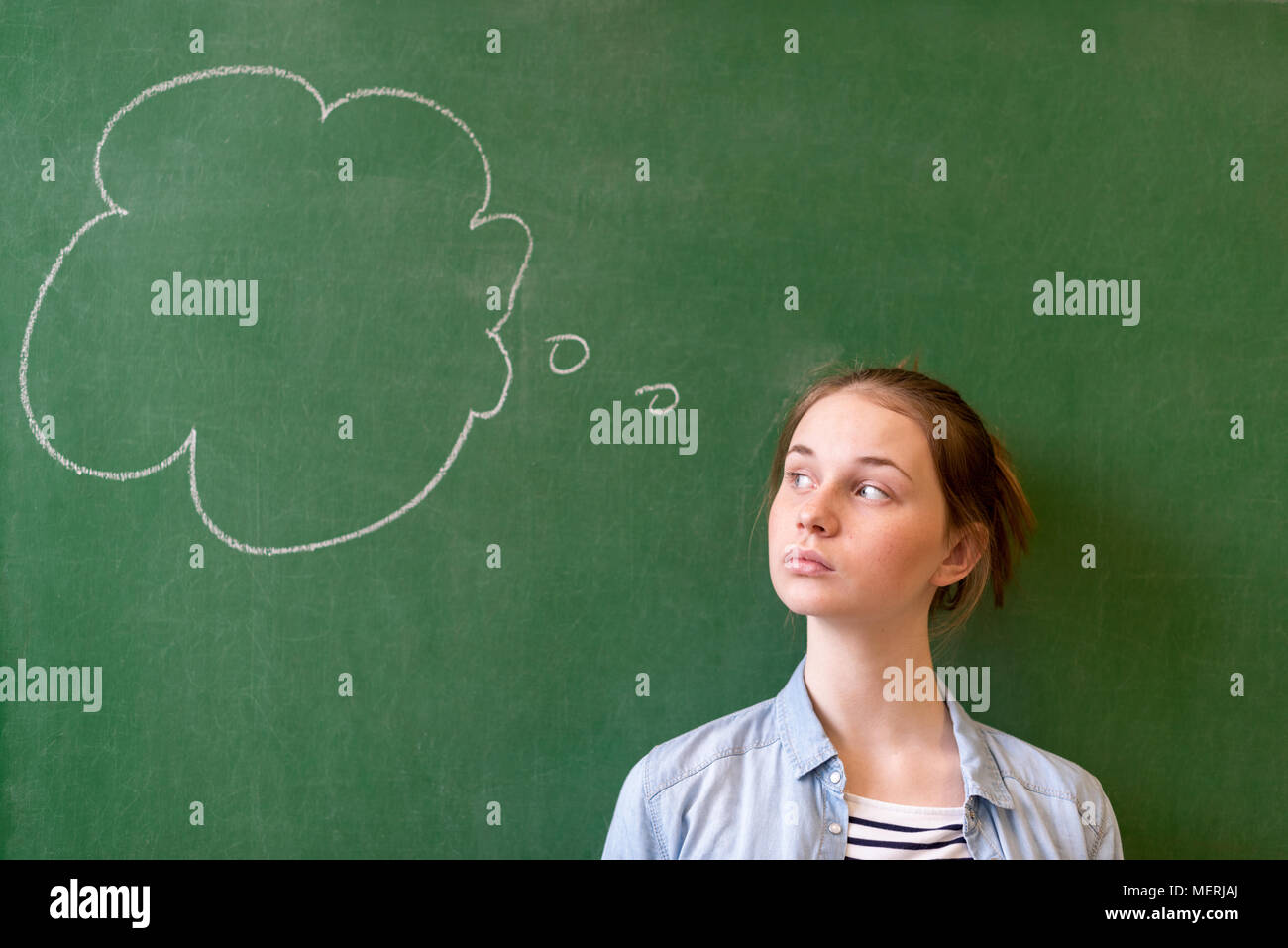 Student thinking blackboard concept. Pensive girl looking at thought bubble on chalkboard background. Caucasian student. Future, profession. Stock Photo
