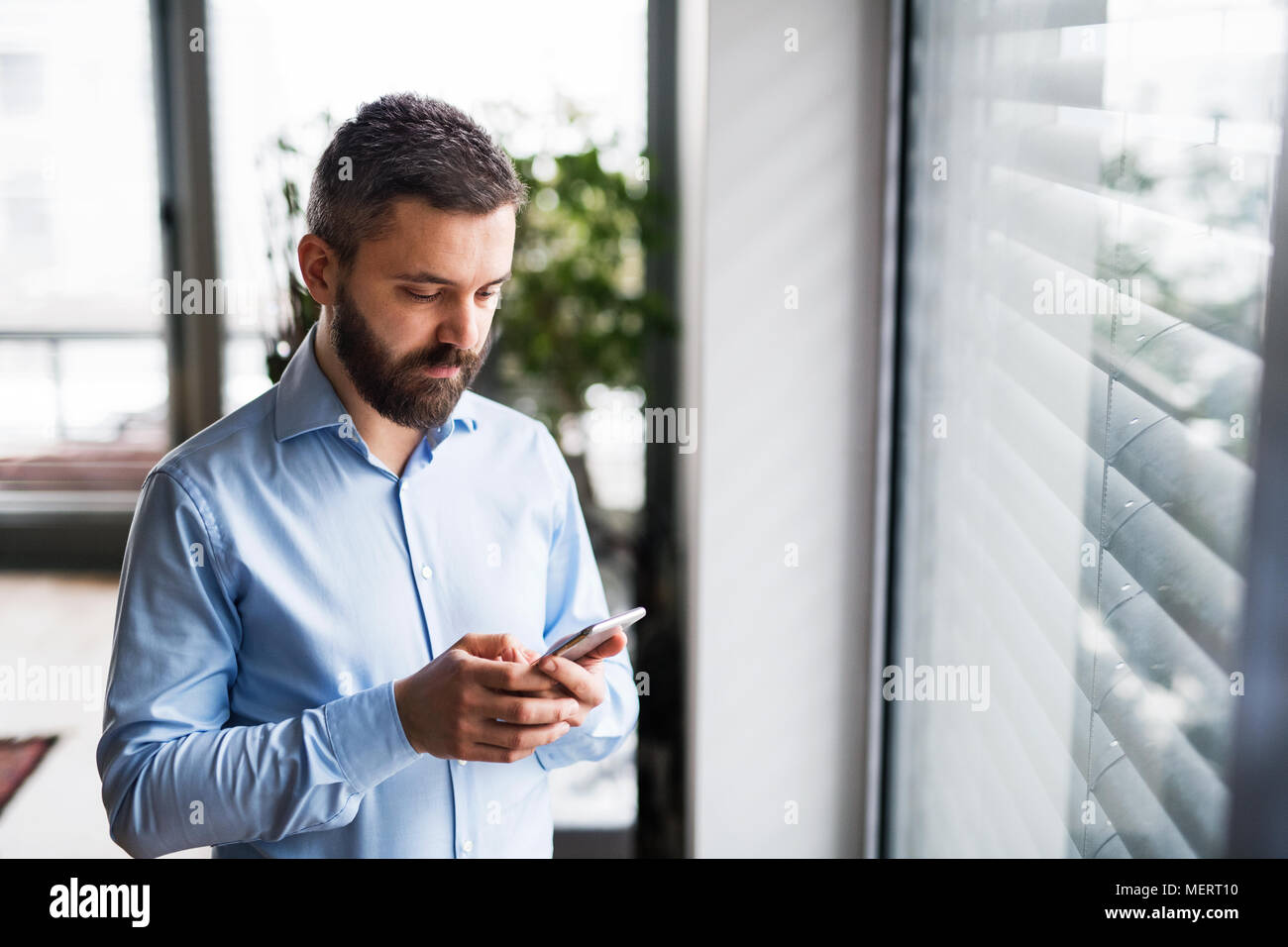 A man with a smartphone by the window, text messaging. Stock Photo