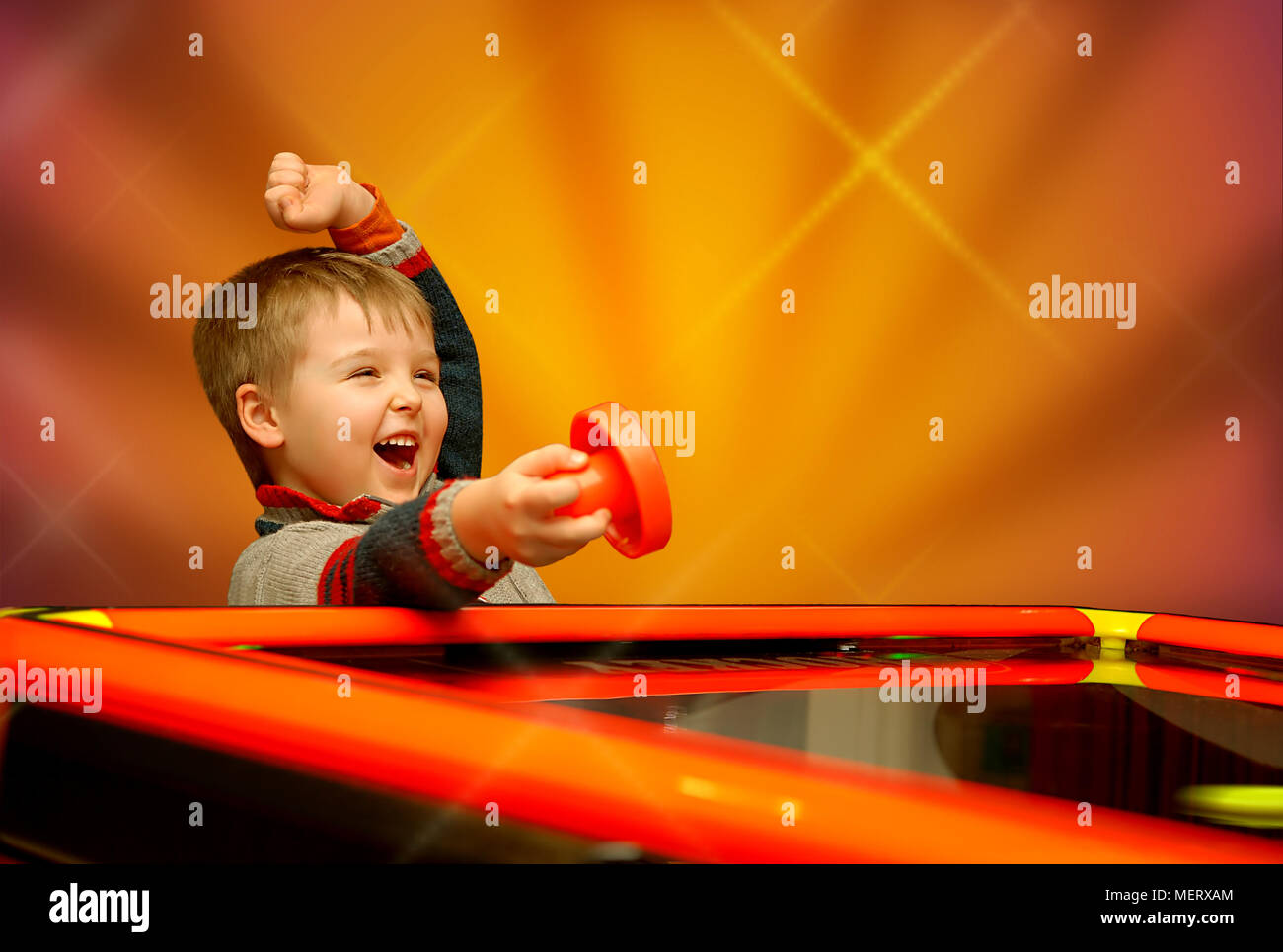 A child who has won his air hockey game, with a red mallet in his hand. Stock Photo