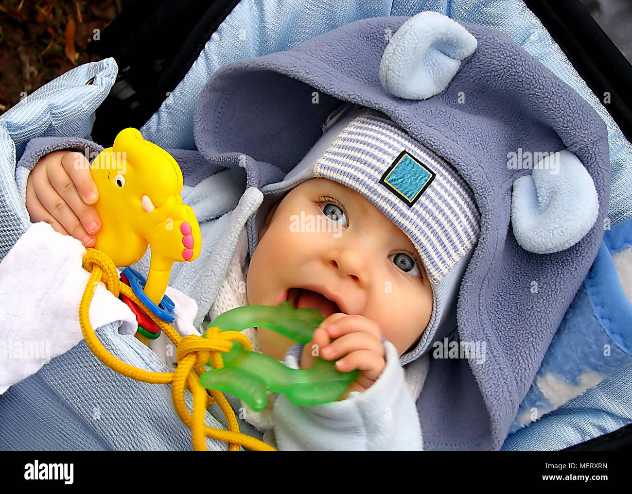 A baby lying and teething a green toy, outdoor. Stock Photo