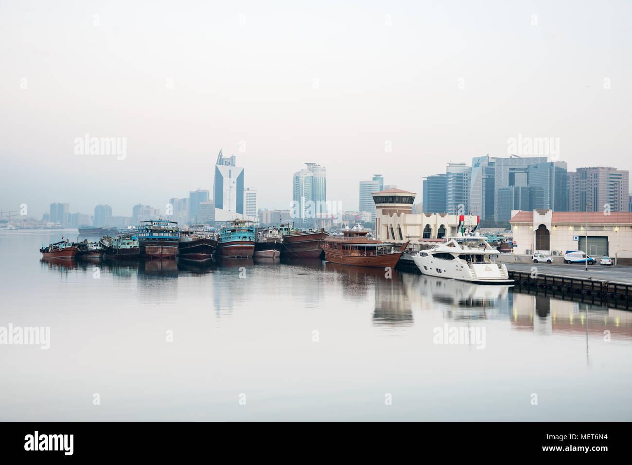looking across Dubai Creek with offices, buildings  and old dhow boat lined in row Stock Photo
