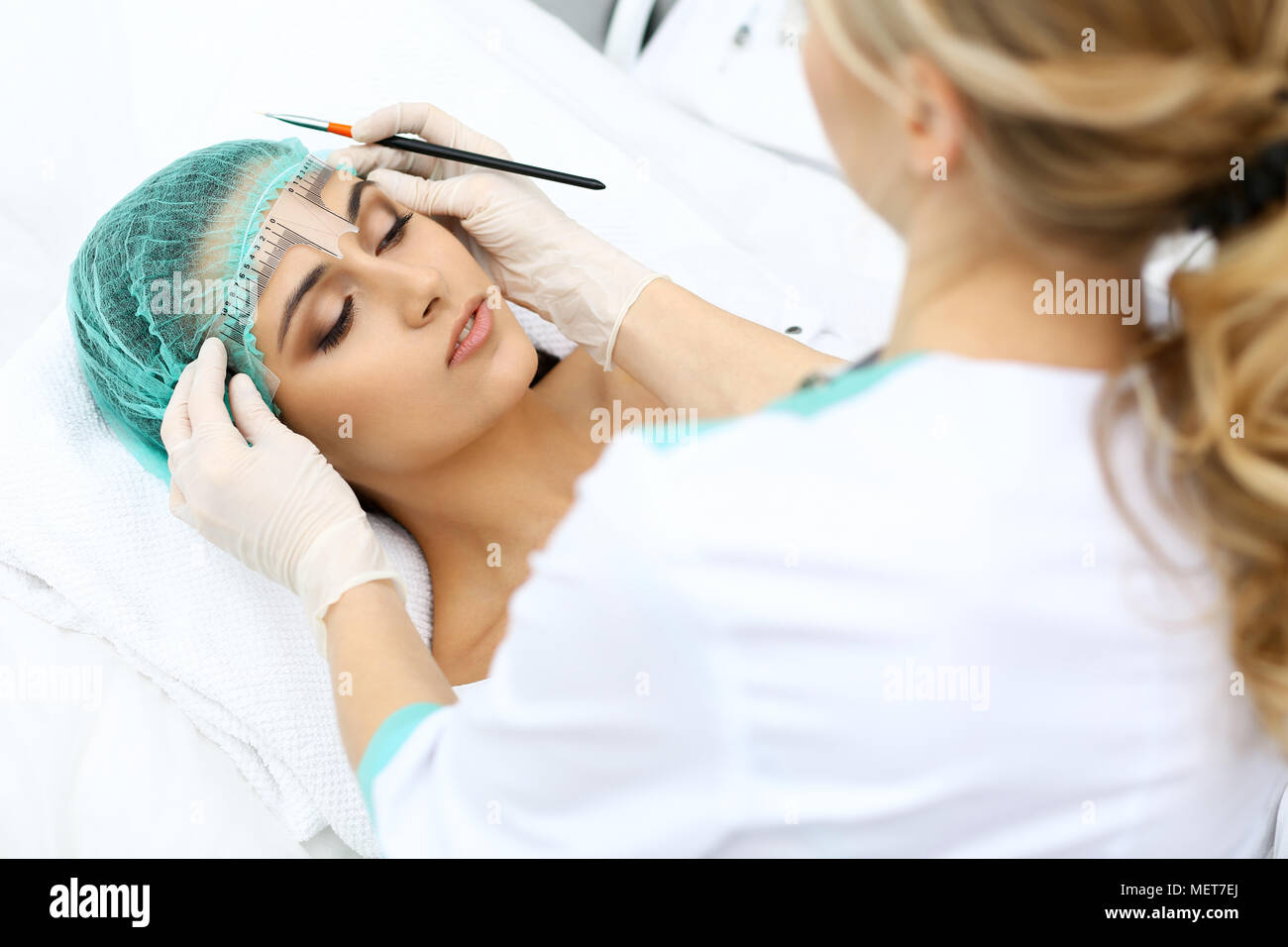 Professional beautician is going to correct eyebrow line at woman face ...