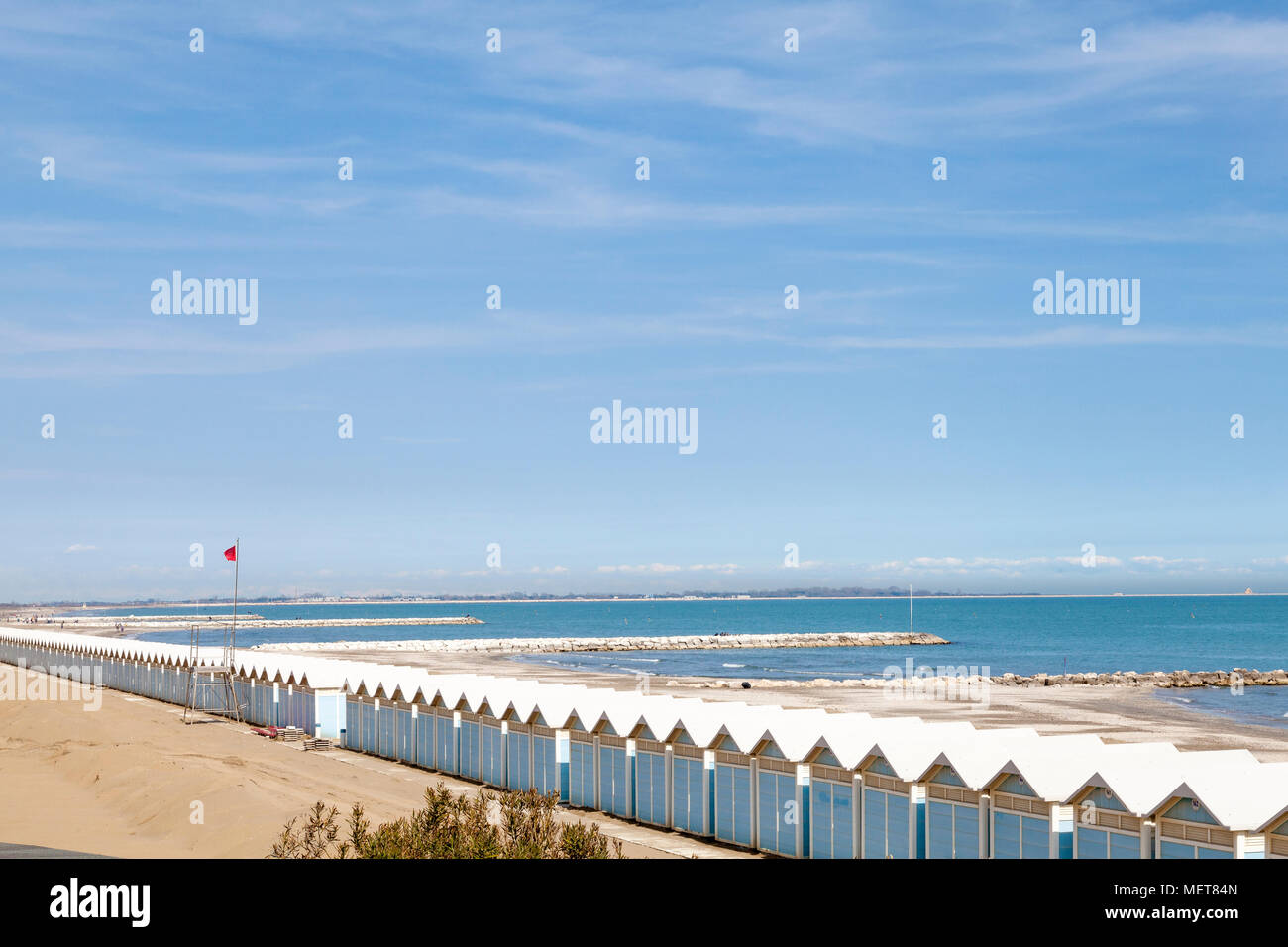 The beach in Lido di Venezia (Venice Lido) with a long line of cabanas (Beach huts), Lido, Venice, Veneto, Italy and a view over the breakwaters in th Stock Photo