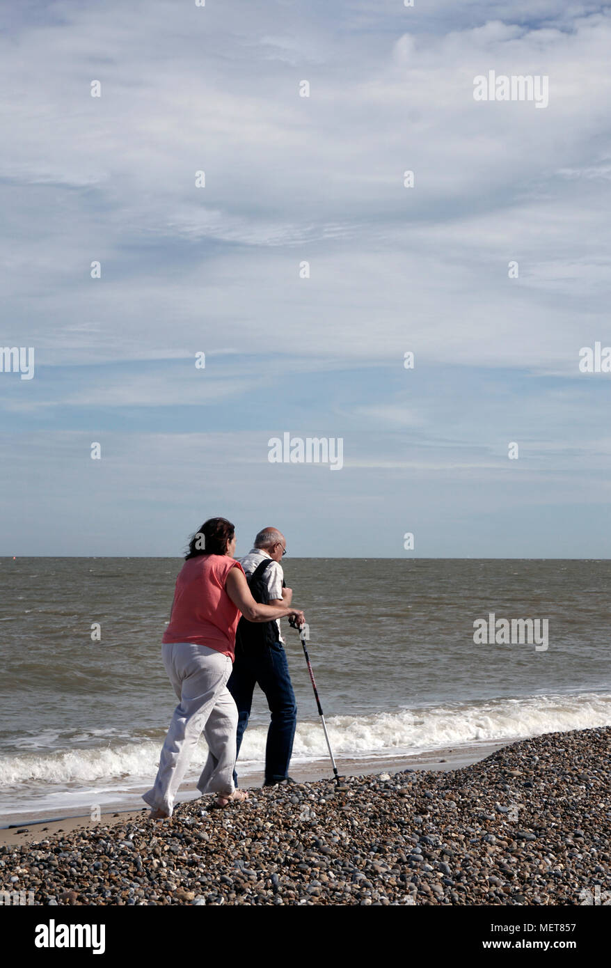 older couple walking along seashore on shingle beach at sizewell suffolk england Stock Photo