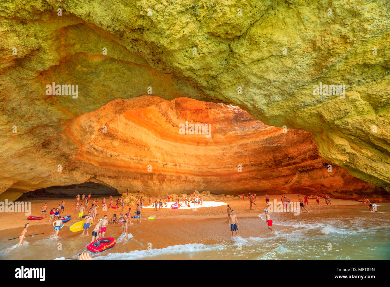 Benagil, Portugal - August 23, 2017: tourists on the sand beach inside sea cave listed in the world's top 10 best caves. People visiting Benagil Cave swimming from Benagil Beach or by boat trip. Stock Photo