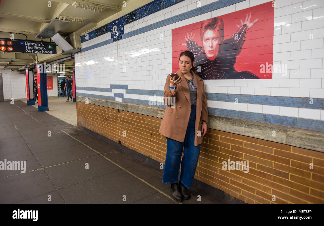 New York, USA. 121 April, 2018. A woman takes a selfie with one of the images of David Bowie on the Bleecker Street platform of the he Broadway-Lafayette subway station.  The installation, sponsorsed  by Spotify, is being held in conjunction with the exhibition "David Bowie IS" at the Brooklyn. The subway installation is just blocks from where the late rock star lived in Soho. The art will be on display until mid May. ©Stacy Walsh Rosenstock Stock Photo