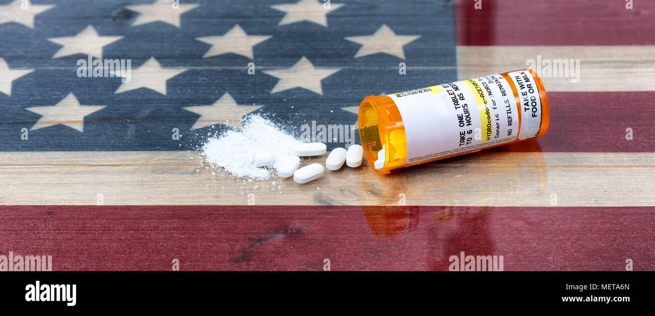 Bottle of prescription for Hydrocodone or generic opioid with crushed or whole pain killer tablets. Rustic USA flag in background for drug addiction c Stock Photo