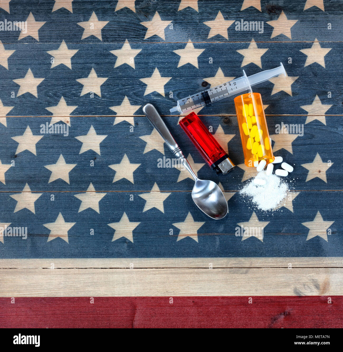 Overhead view of opioid pain killer tablets with spoon, lighter and syringe on rustic USA flag in background for drug addiction concept in America Stock Photo