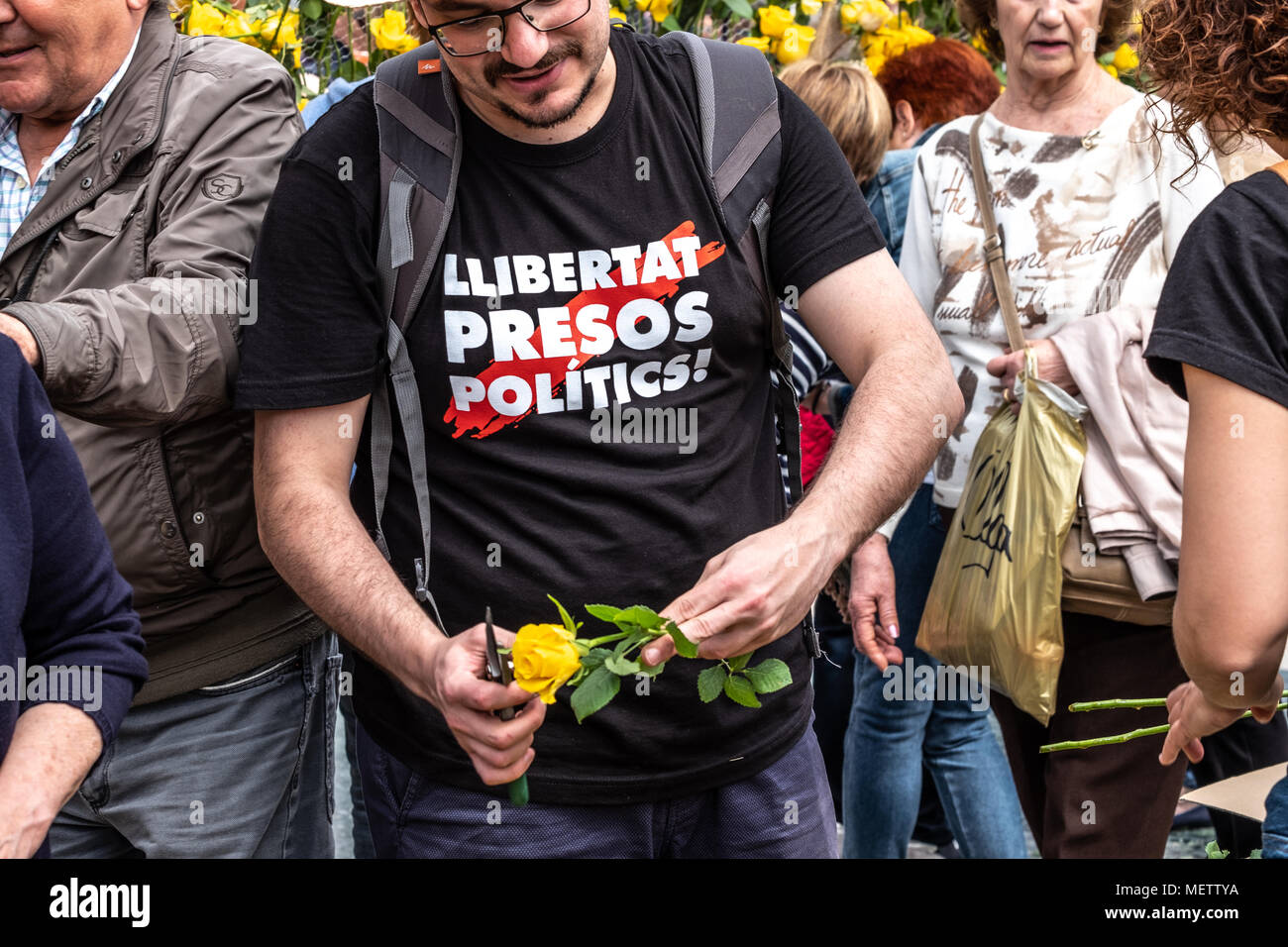 Barcelona, Spain. 23rd April, 2018. A young man is seen preparing yellow roses wearing a T-shirt to support political prisoners. Catalunya celebrates the 'Day of Sant Jordi', the day of books and roses. Catalunya hopes to reach the figure of 7 million roses sold. It is tradition to give a rose or a book among lovers. Numerous literary authors sign their books to the public on the street. Credit: SOPA Images Limited/Alamy Live News Stock Photo