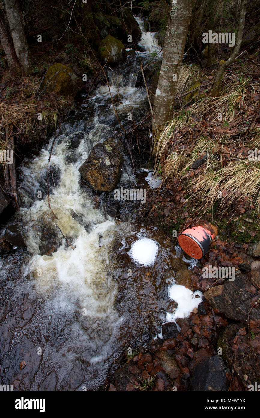 Waste water running from a pipe is causing a frothy foam on the surface of a forest creek. Stock Photo