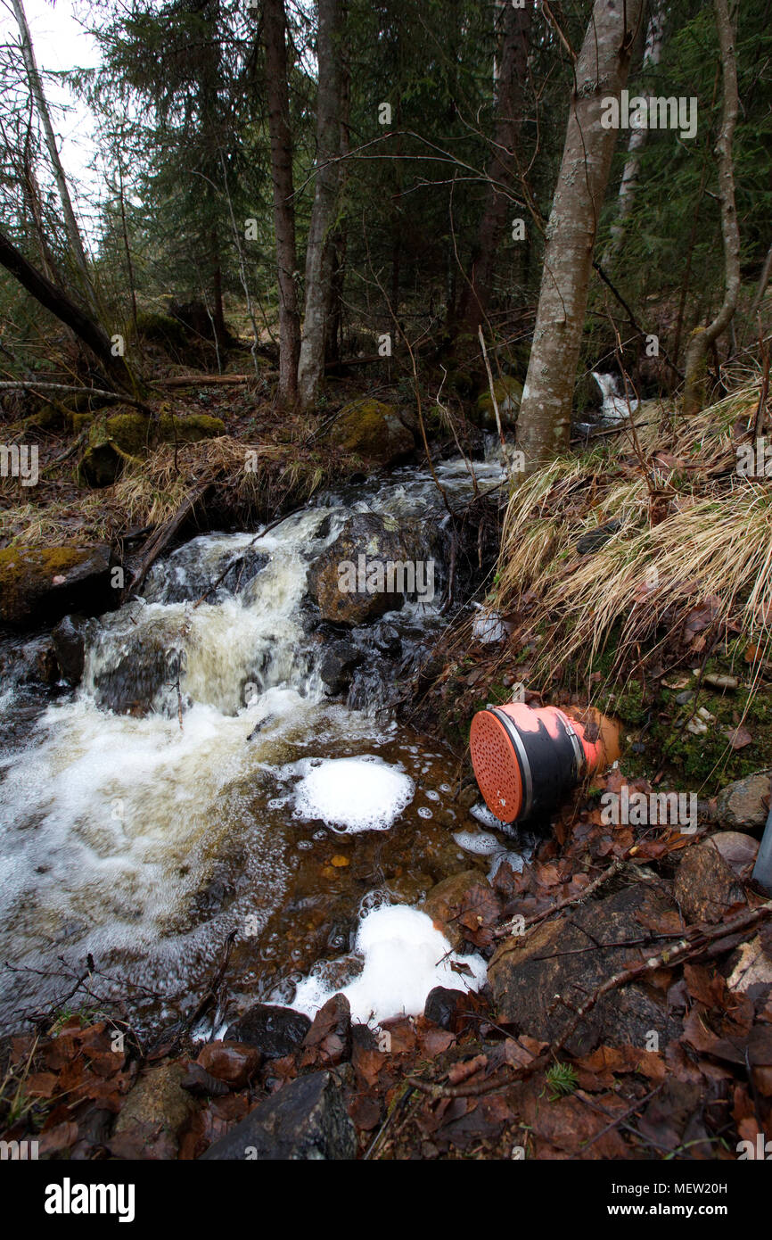 Waste water running from a pipe is causing a frothy foam on the surface of a forest creek. Stock Photo