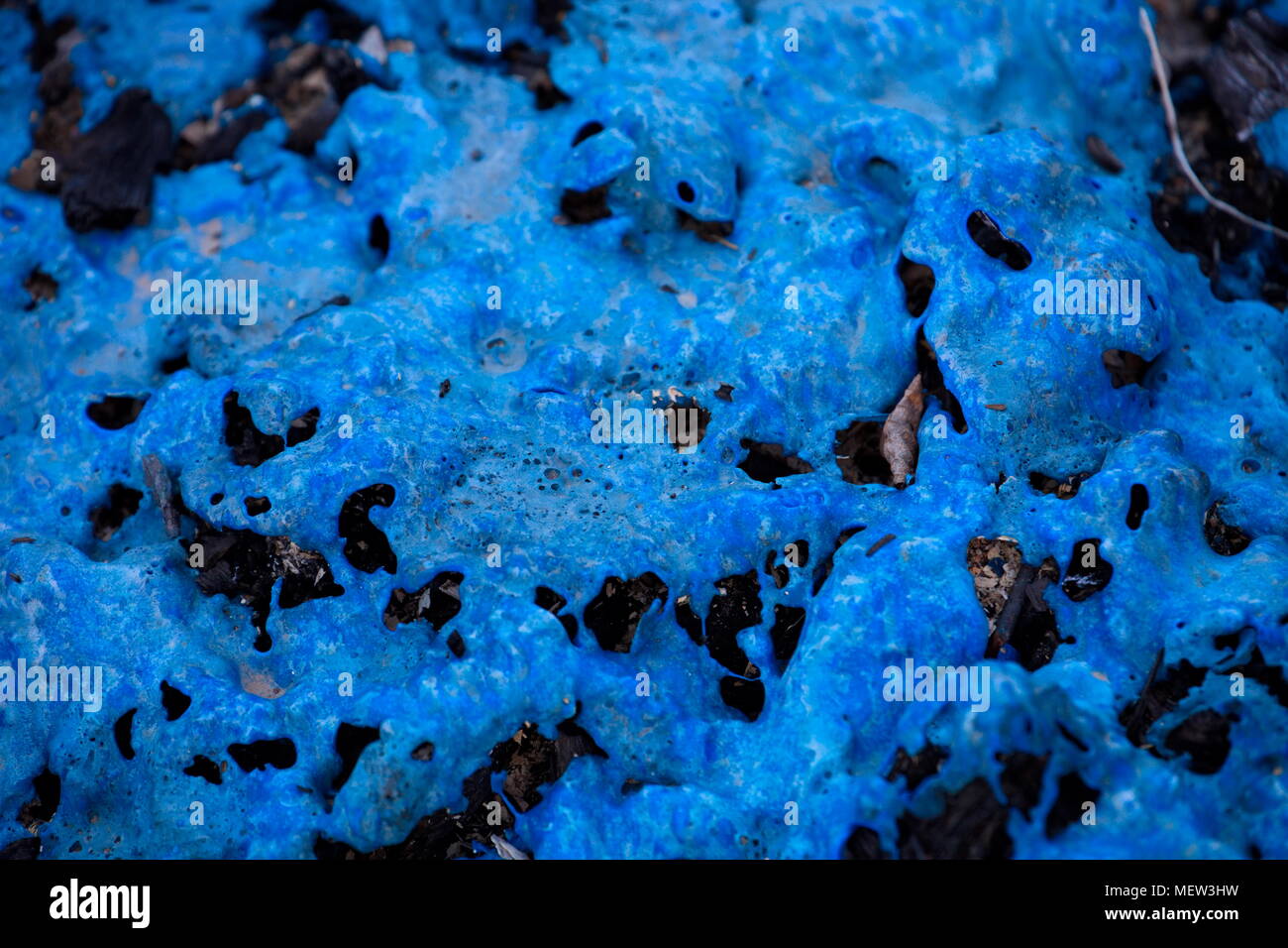 Blue melted plastic is covering a burned up garbage heap Stock Photo