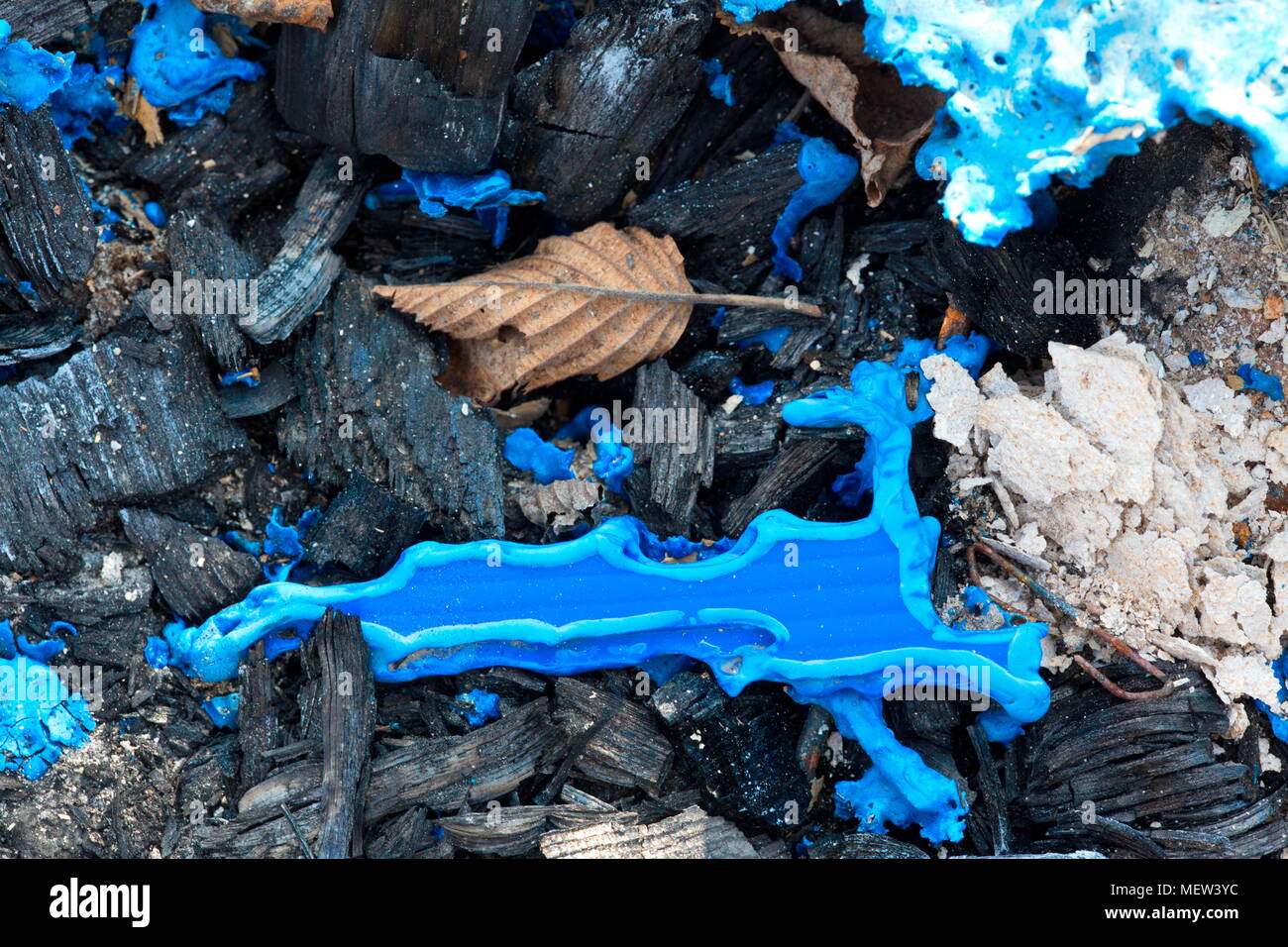 Blue melted plastic is covering a burned up garbage heap Stock Photo