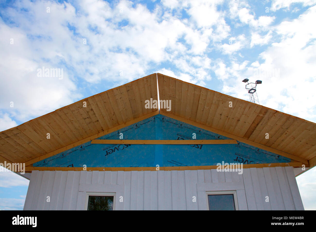 A small wooden house is under construction, the blue insulation sheeting is visible under the roof. Stock Photo