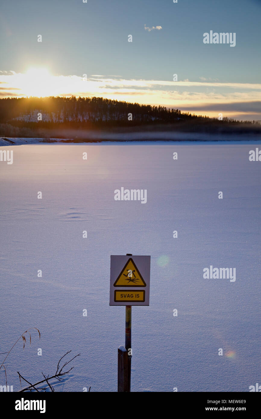 Frozen lake at dusk with a  sign warning in Swedish to walk on the thin ice. Stock Photo