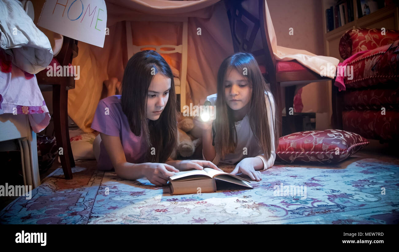 Portrait of two girls in pajamas lying on floor at bedroom and reading book at night Stock Photo
