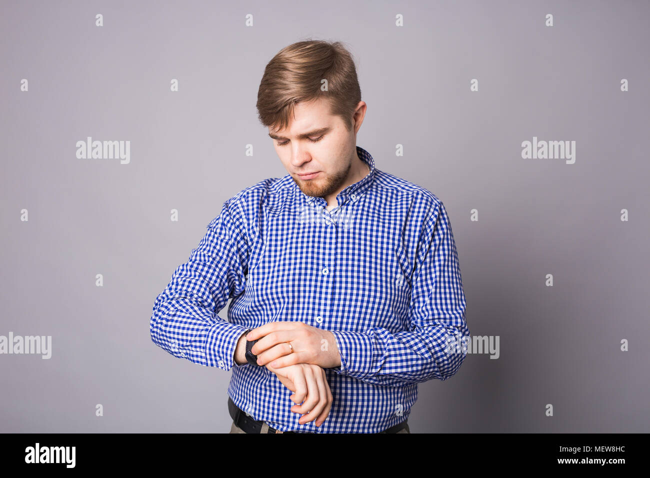 Young man looking his wrist watch over gray background Stock Photo