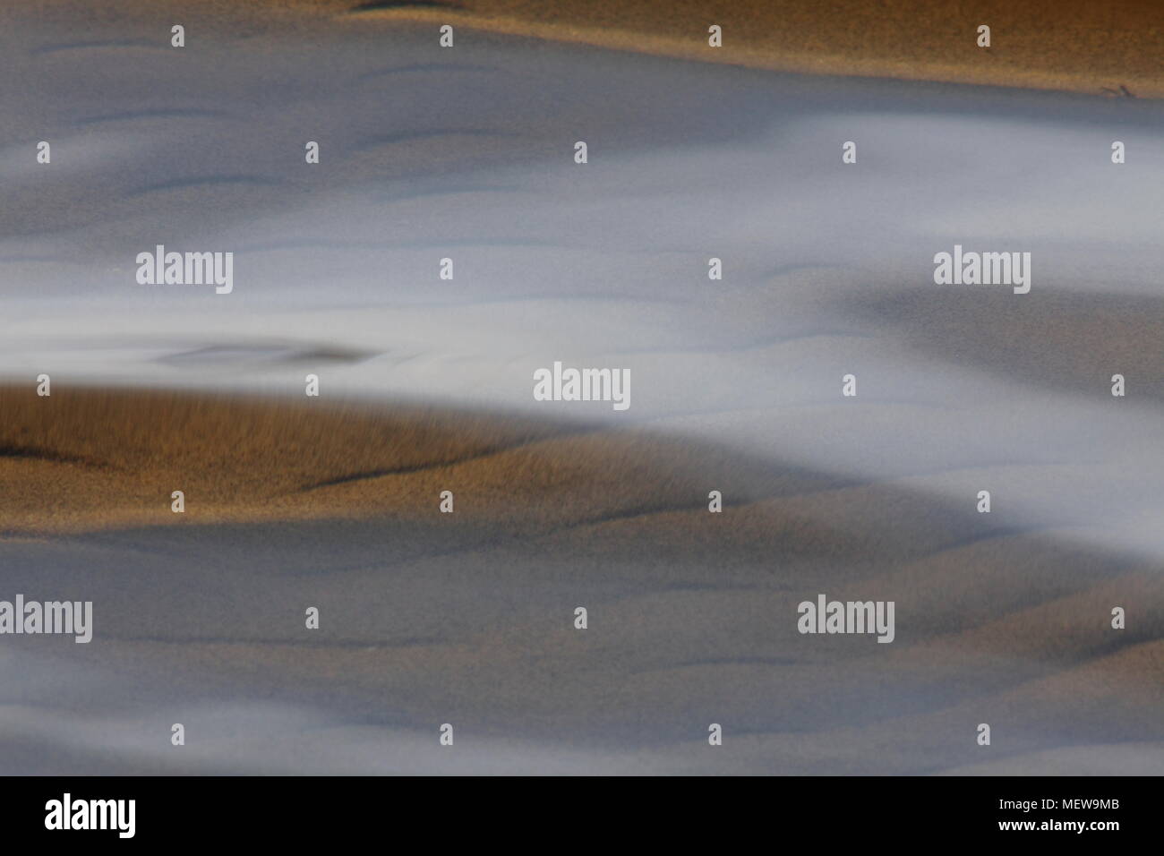 The sandy ground of a lake is shining through the clear rippling water of a shallow lake Stock Photo