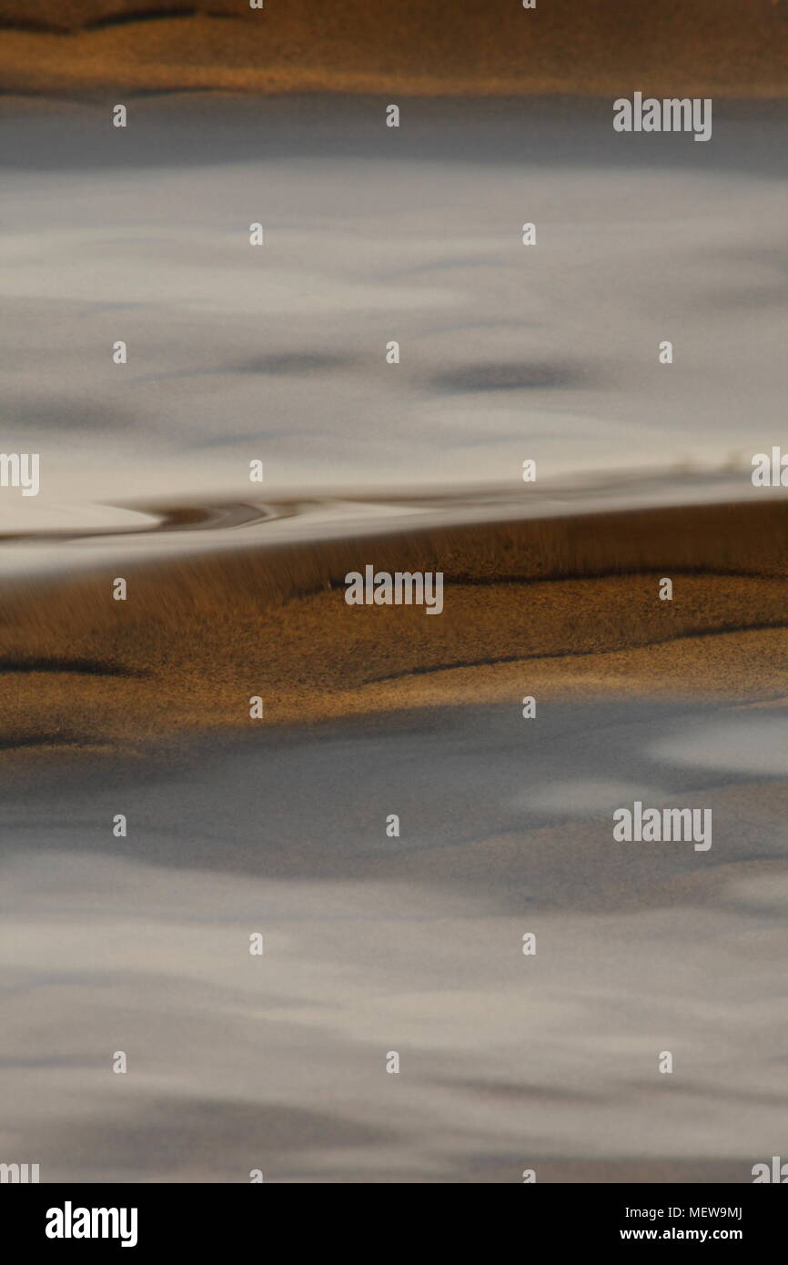 The sandy ground of a lake is shining through the clear rippling water of a shallow lake Stock Photo