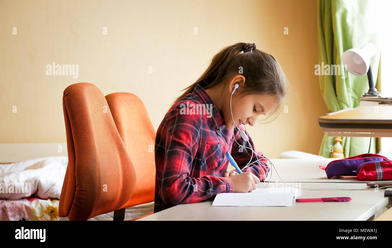 Portrait of smiling teenage girl doing homework and listening music ...