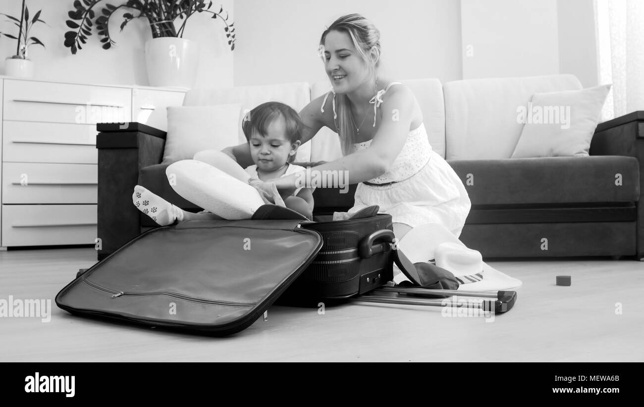 Cute smiling toddler boy sitting in suitcase while mother packing things for traveling Stock Photo