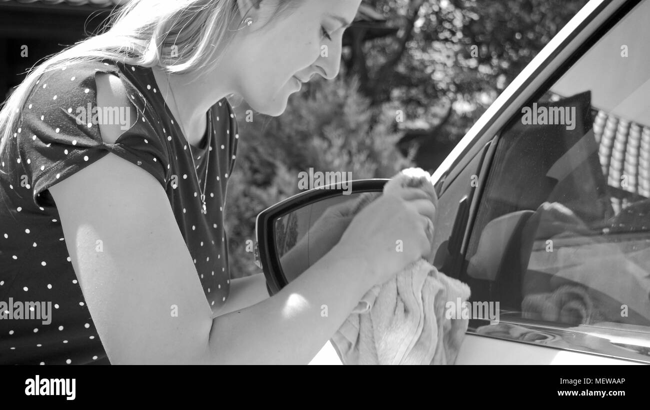Black and white portrait of young female driver cleaning car side