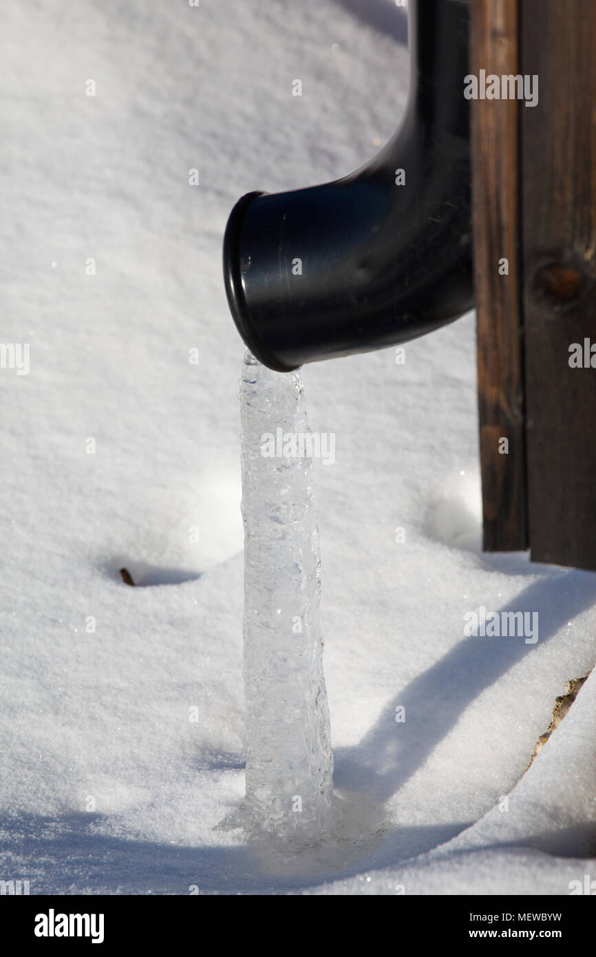 A stream of ice is emerging from a roof drain pipe on a cold winter day. Stock Photo