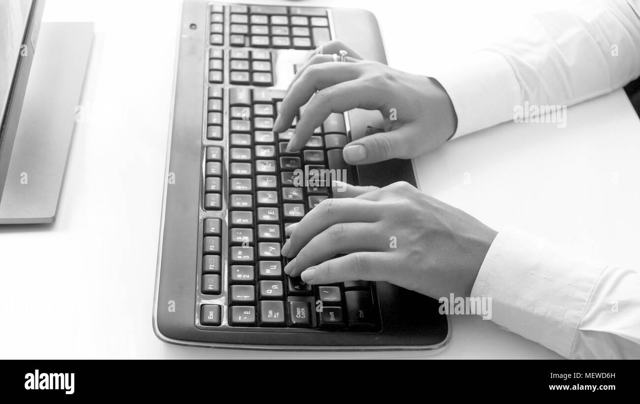 Black and white photo of young woman typing text on computer keyboard