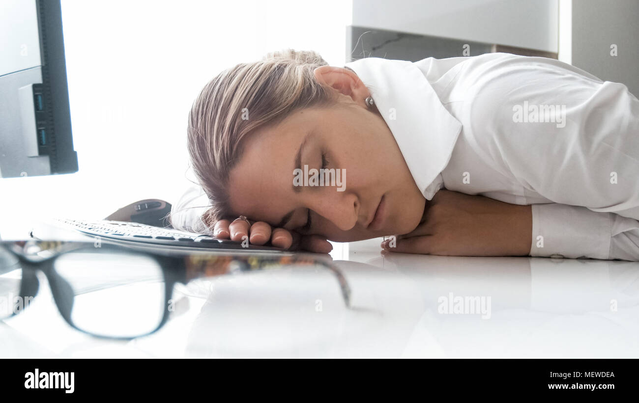 Portrait of exhausted young businesswoman sleeping on desk at office ...